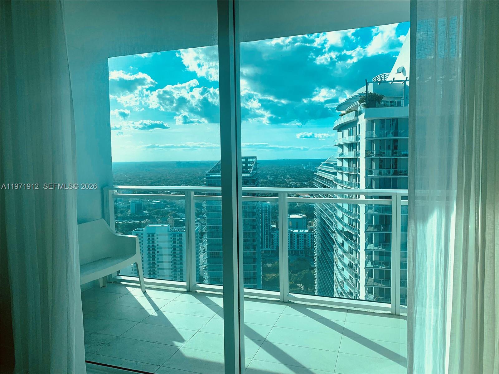 A balcony with a white chair overlooks a city skyline with multiple high-rise buildings — 1080 Brickell Ave # 4009, Miami FL 33131, MIAMI, FL