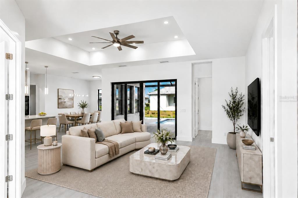 A bright living room with a tray ceiling, neutral furniture, and sliding glass doors to a pool — 17315 CAPE HORN BOULEVARD, PUNTA GORDA, FL