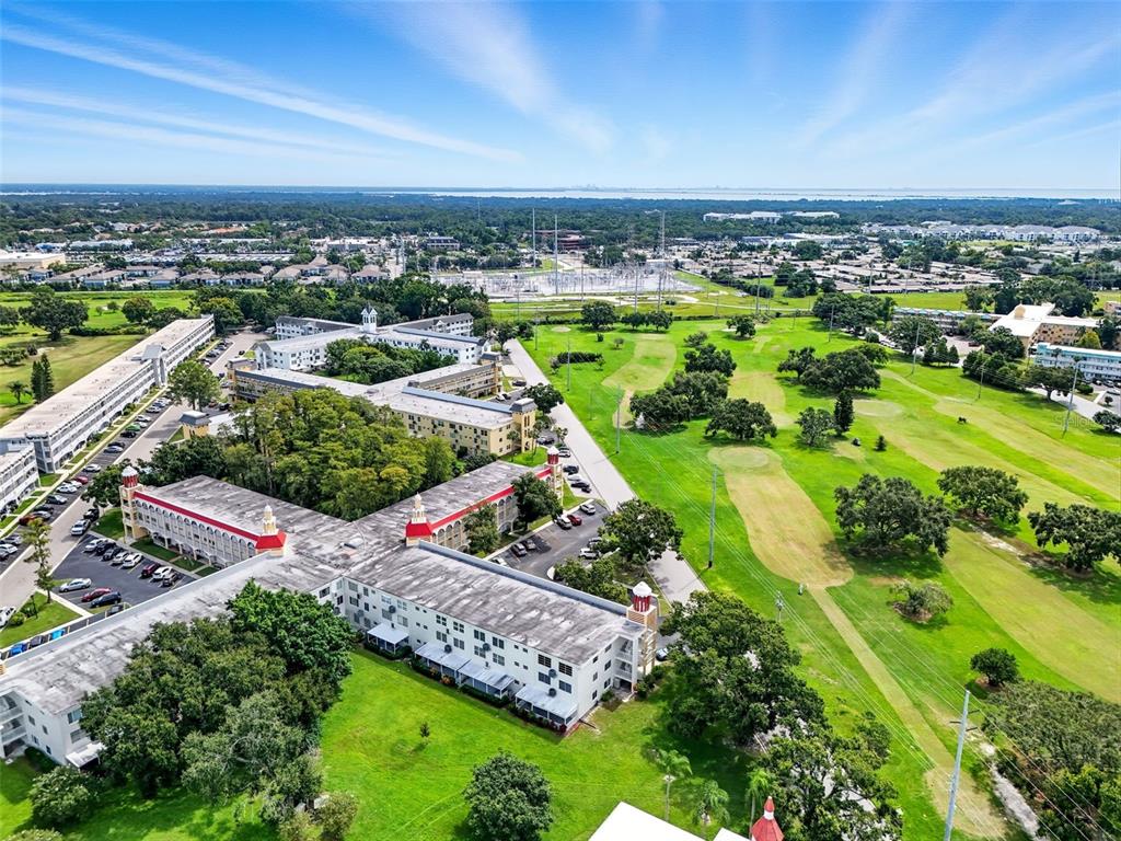 An aerial view shows multi-story apartment buildings situated next to a large green golf course — 2430 FLORENTINE WAY UNIT 56, CLEARWATER, FL