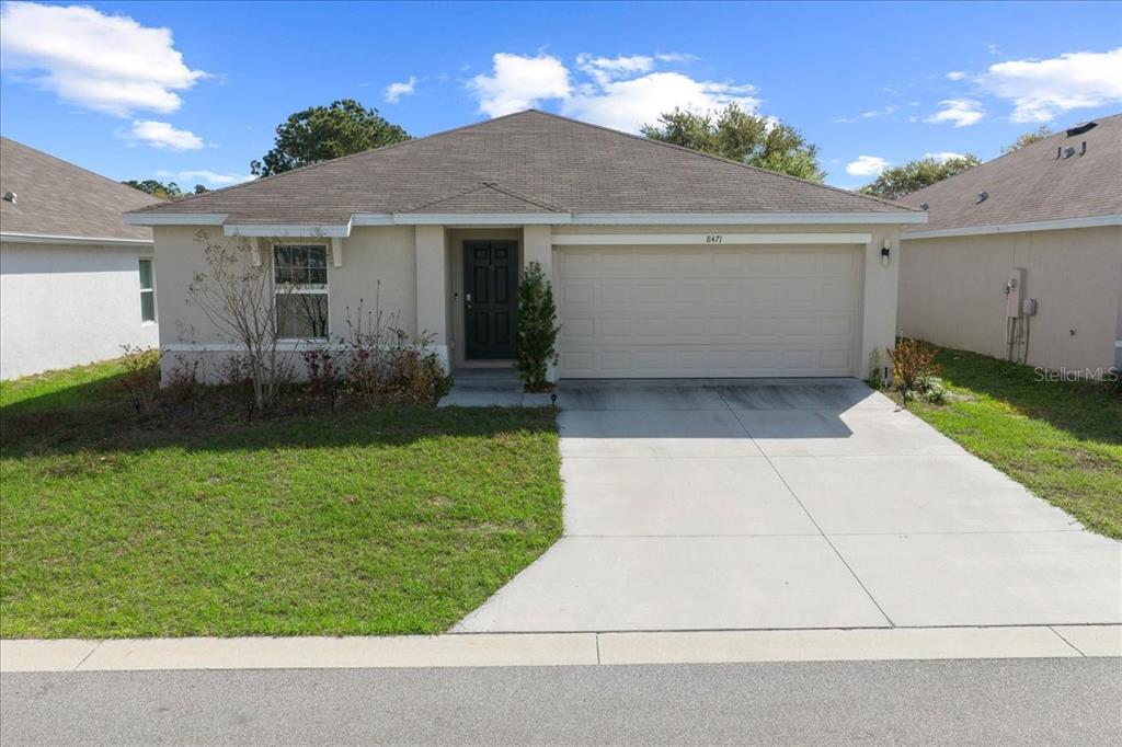 A single-story house with a beige stucco exterior, a two-car garage, and a concrete driveway — 8471 CLEARWAY DRIVE, WILDWOOD, FL