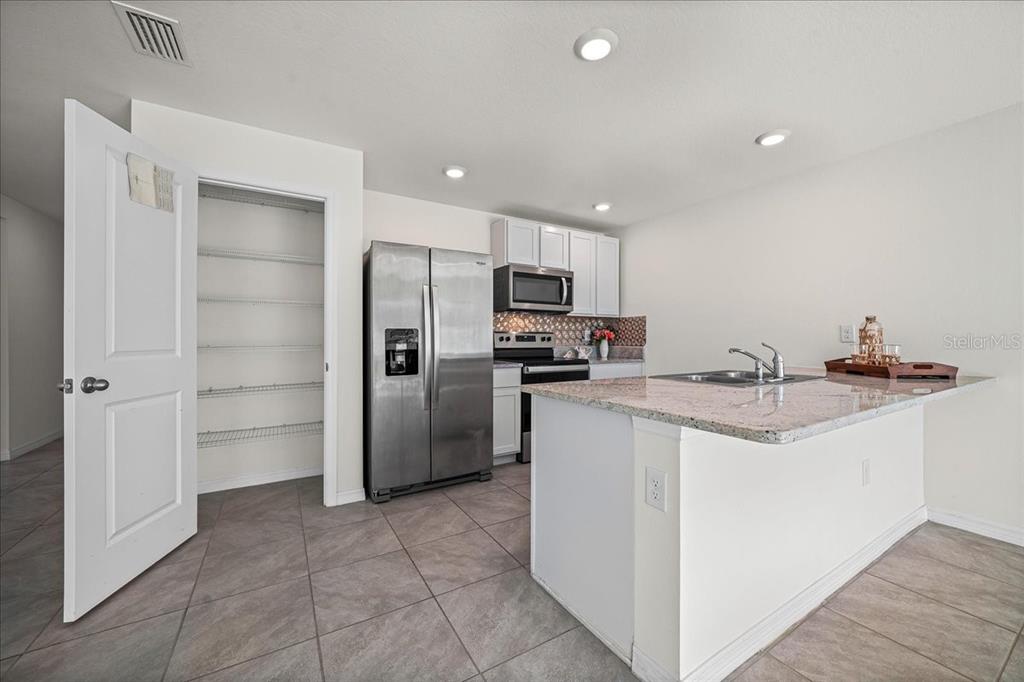 A kitchen features a pantry, stainless steel appliances, white cabinets, and a granite-topped island — 8471 CLEARWAY DRIVE, WILDWOOD, FL
