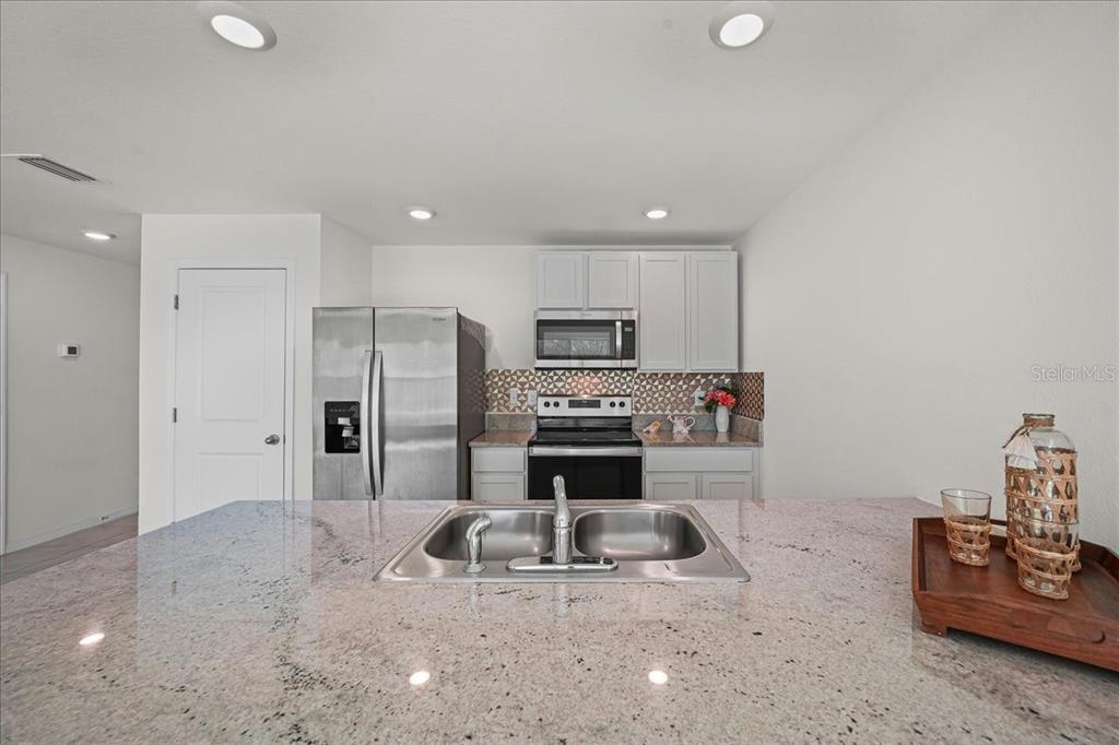 A kitchen features light-colored cabinets, stainless steel appliances, a granite countertop, and a double sink — 8471 CLEARWAY DRIVE, WILDWOOD, FL