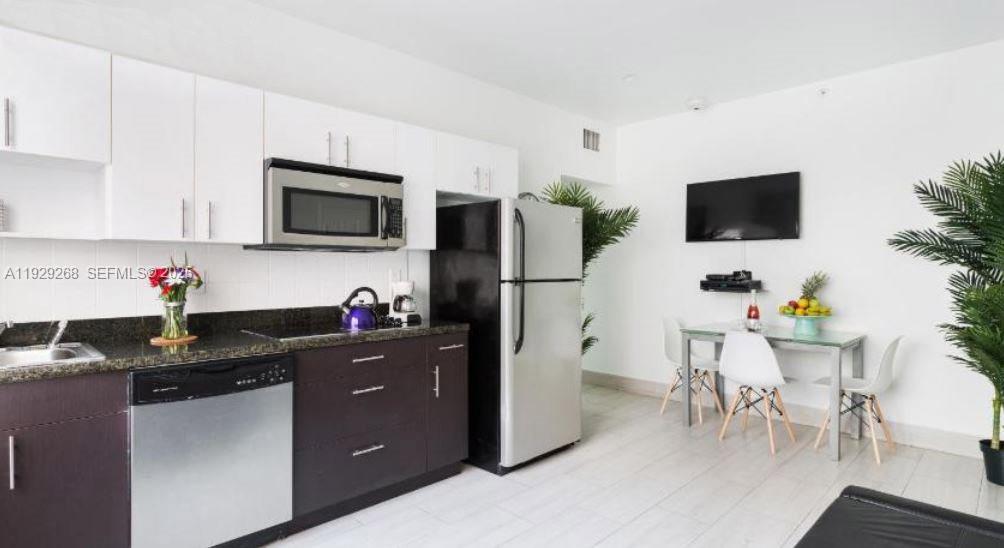 A kitchen with dark cabinets, stainless steel appliances, and a small dining area with chairs — 1355 Drexel Ave, Miami Beach FL 33139, MIAMI BEACH, FL