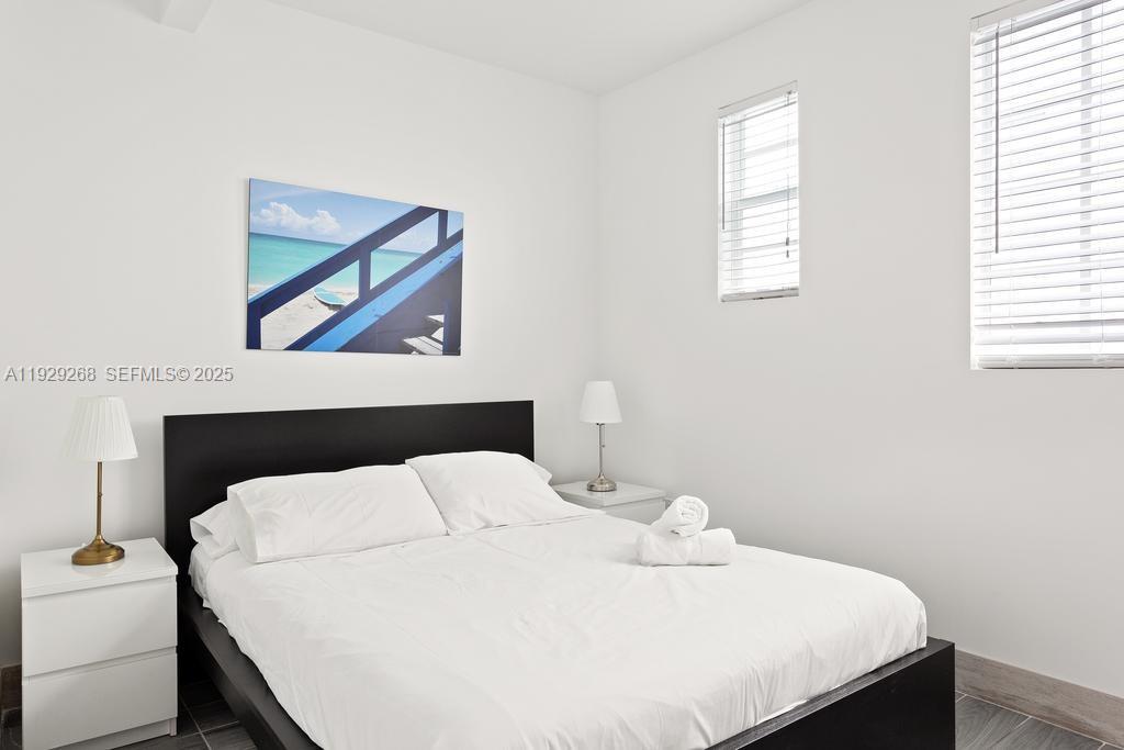 A bedroom features a bed with white linens, a black headboard, and two bedside lamps — 1355 Drexel Ave, Miami Beach FL 33139, MIAMI BEACH, FL