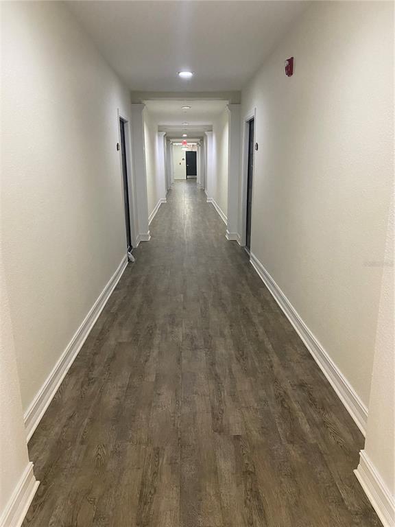 A long, narrow apartment hallway features light-colored walls, white trim, and wood-look flooring — 5550 E MICHIGAN STREET UNIT 1306, ORLANDO, FL