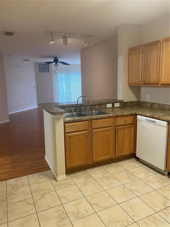 A kitchen with wood cabinets, laminate countertops, and tile flooring opens to a living area — 5550 E MICHIGAN STREET UNIT 1306, ORLANDO, FL