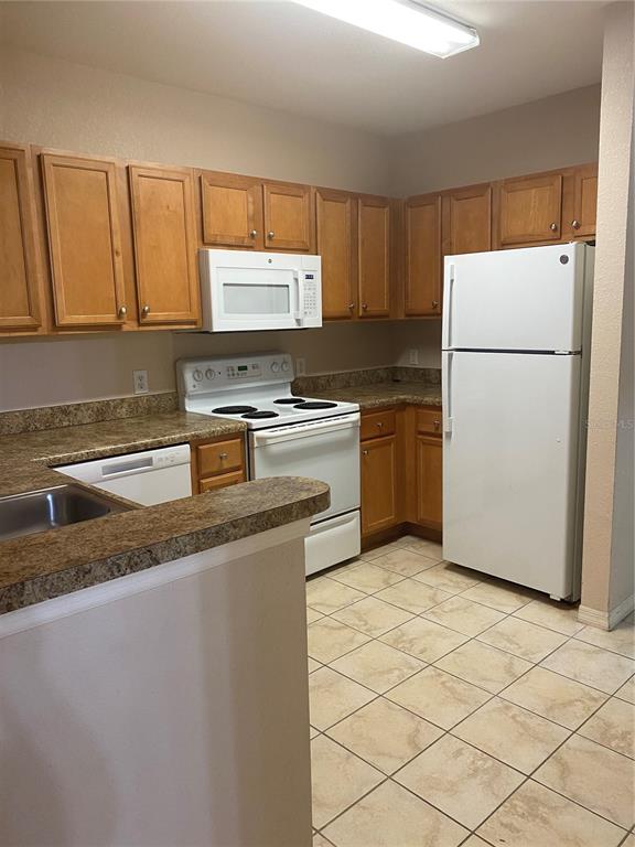 A kitchen features wood cabinets, white appliances, laminate countertops, and light-colored tile flooring — 5550 E MICHIGAN STREET UNIT 1306, ORLANDO, FL