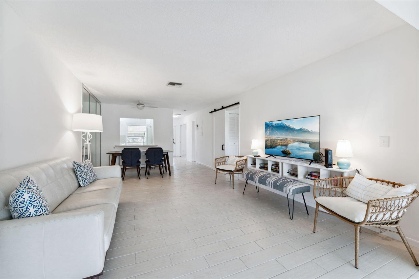 A bright living room features white tile flooring, a white sofa, and a television console — 1120 Cactus Terrace # c, Delray Beach FL 33445, DELRAY BEACH, FL