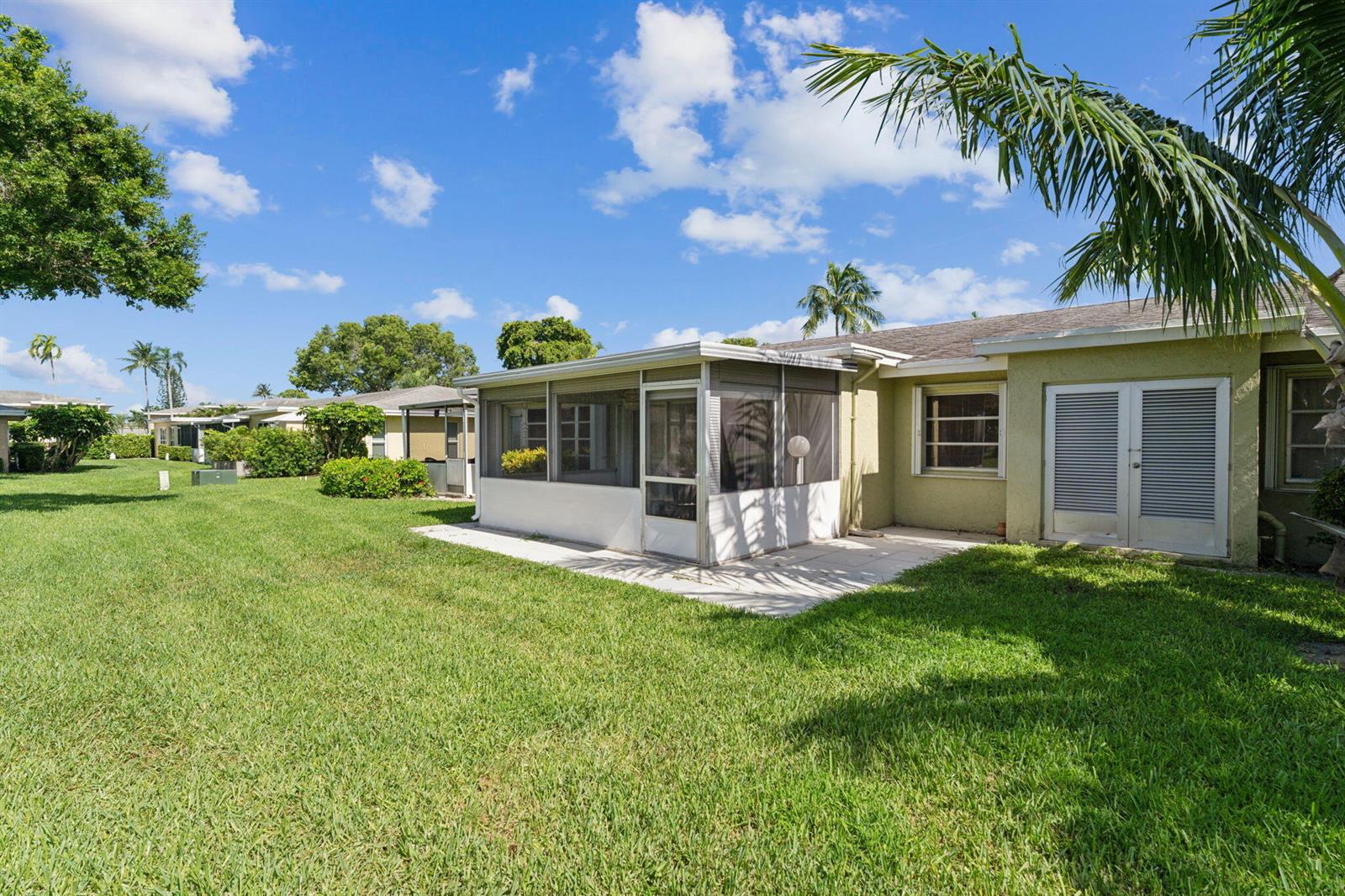 A backyard view of a house with a screened-in patio and a large grassy lawn — 1120 Cactus Terrace # c, Delray Beach FL 33445, DELRAY BEACH, FL