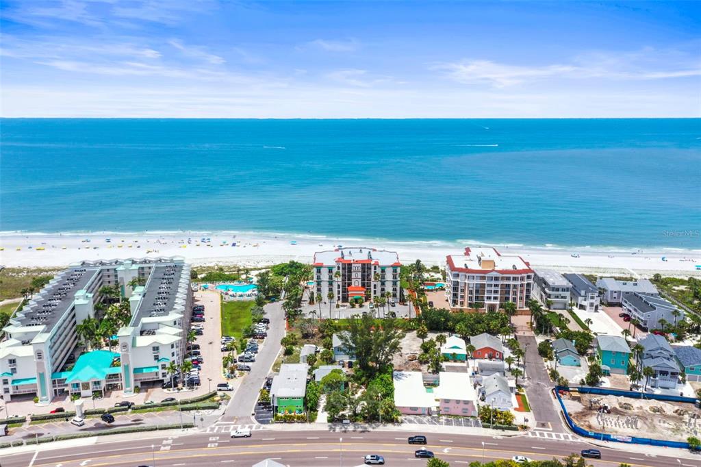 An aerial view shows beachfront condominiums, a parking lot, and a road near the ocean — 200 121ST AVENUE UNIT 103, TREASURE ISLAND, FL