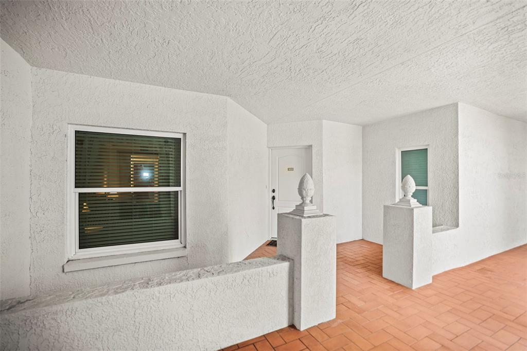 A white stucco exterior entryway features a tiled floor, two decorative finials, and a window — 200 121ST AVENUE UNIT 103, TREASURE ISLAND, FL