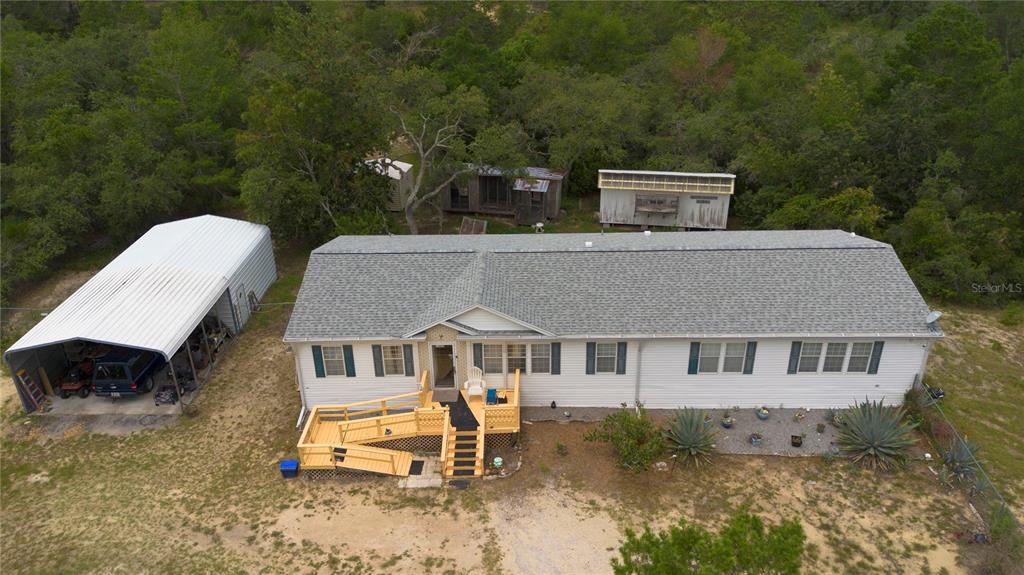 An aerial view shows a white manufactured home with a metal carport and wooden deck — 13020 WEBSTER STREET, BROOKSVILLE, FL