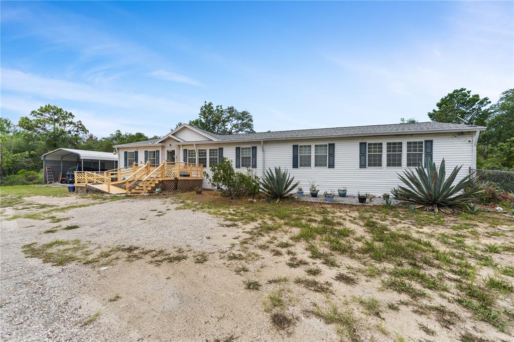 A single-story manufactured home with a wooden deck, wheelchair ramp, and metal carport — 13020 WEBSTER STREET, BROOKSVILLE, FL