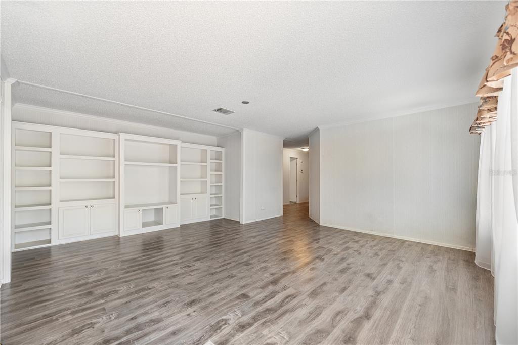 A living room with gray wood-look flooring, white walls, and a large built-in shelving unit — 13020 WEBSTER STREET, BROOKSVILLE, FL