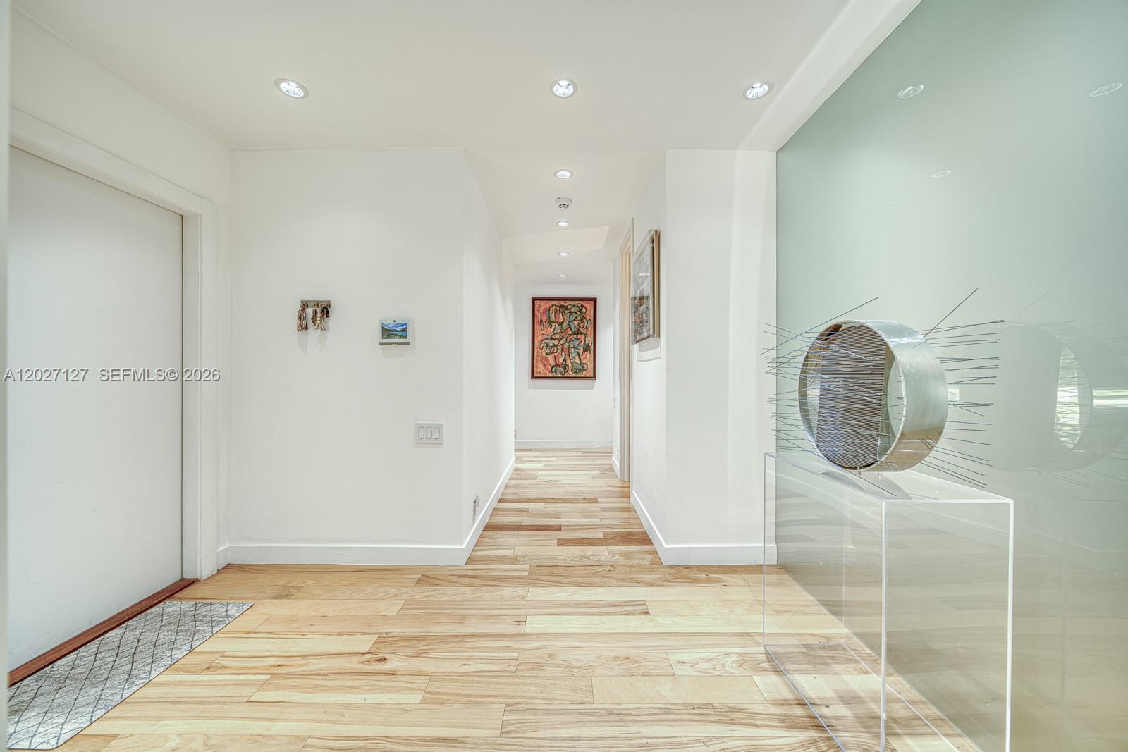 A bright hallway features light wood flooring, white walls, recessed lighting, and modern art pieces — 620 Conde Ave, Coral Gables FL 33156, CORAL GABLES, FL