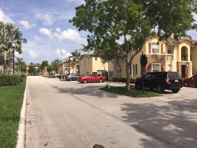 A paved road leads past residential buildings, parked cars, and trees under a blue sky — 3360 NE 14th Dr # 30, Homestead FL 33033, HOMESTEAD, FL