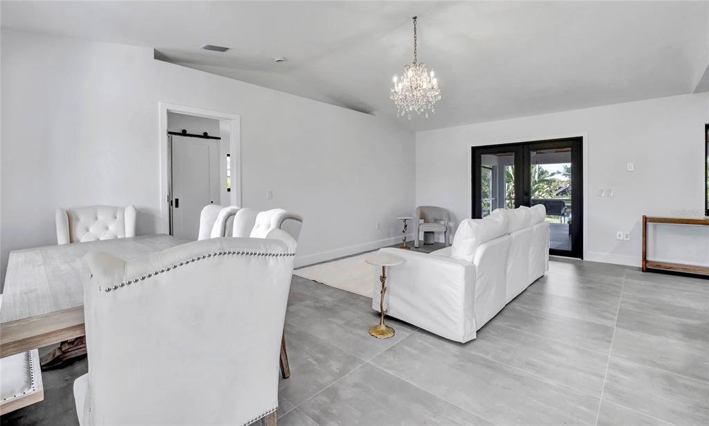 A bright, open-concept living and dining area features white furniture, tile flooring, and a chandelier — 15180 LYNEBURG AVENUE, PORT CHARLOTTE, FL