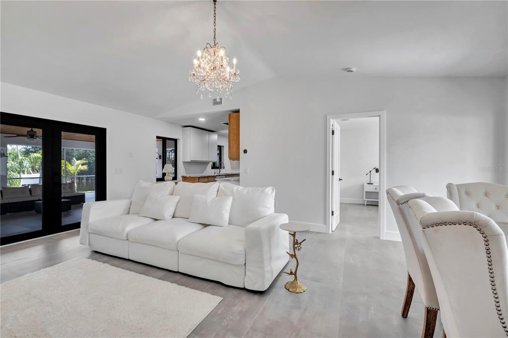 A white sofa sits in a living room with gray tile floors and a chandelier — 15180 LYNEBURG AVENUE, PORT CHARLOTTE, FL