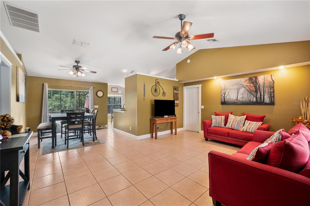A living room and dining area with tile floors, red sofas, and vaulted ceilings — 11724 CONSTANCE WAY, CLERMONT, FL