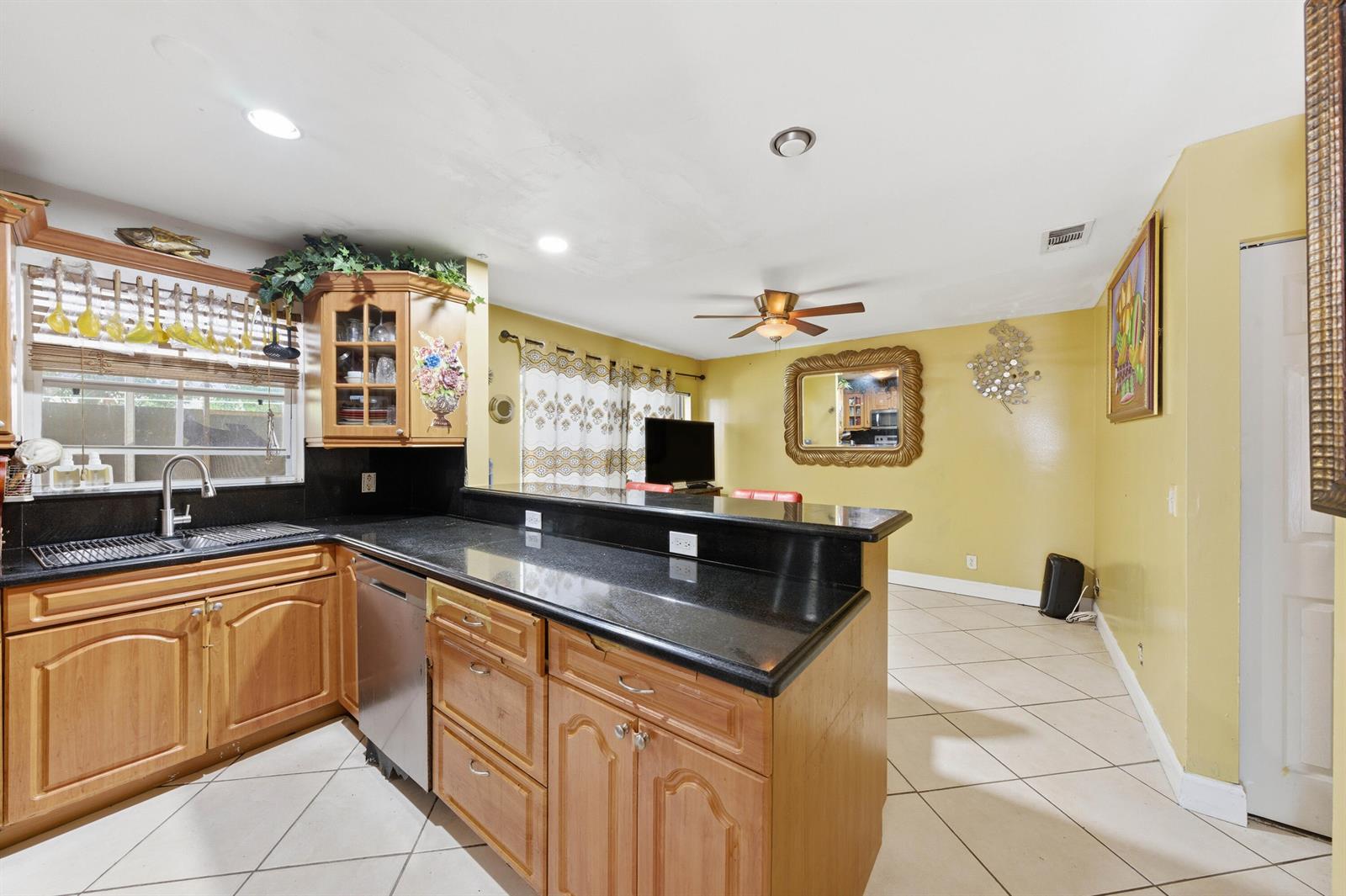 A kitchen with wooden cabinets, black countertops, and tile flooring opens into a yellow living area — 6582 Bayfront Drive, Margate FL 33063, MARGATE, FL