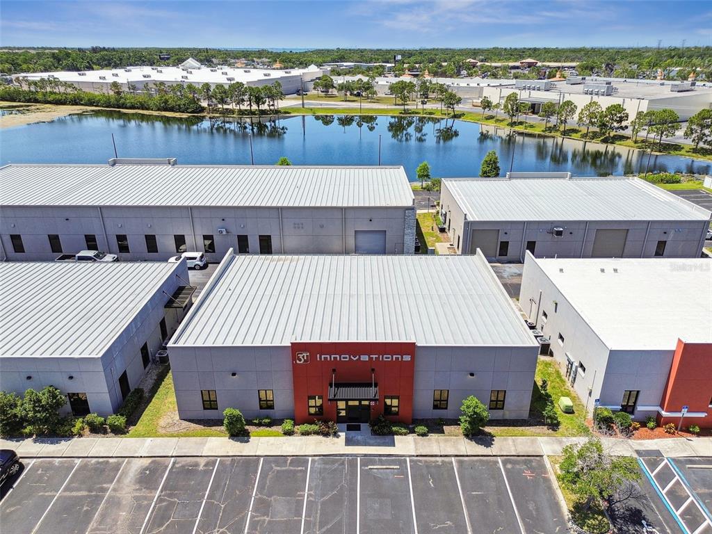 An aerial view shows a commercial building with a red facade and a parking lot — 13908 MONROES BUSINESS PARK, TAMPA, FL