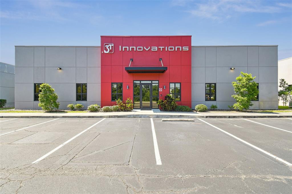 A commercial building with a red central entrance and gray panels sits behind a parking lot — 13908 MONROES BUSINESS PARK, TAMPA, FL