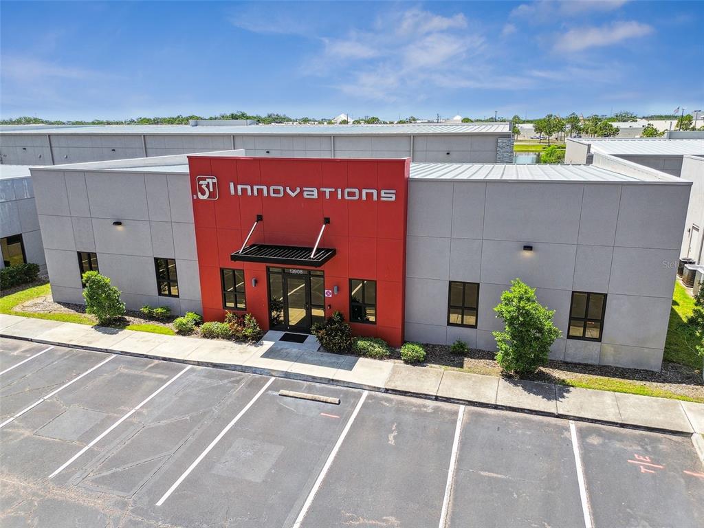 An exterior view of a commercial building with a red entrance and parking lot — 13908 MONROES BUSINESS PARK, TAMPA, FL