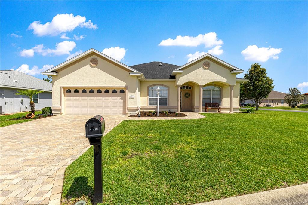 A single-story house with a beige stucco exterior, a two-car garage, and a paved driveway — 12271 SE 175TH LANE, SUMMERFIELD, FL