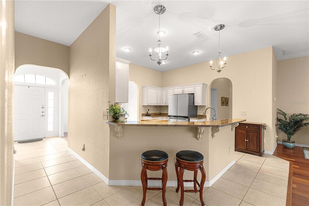 A kitchen with white cabinets, granite countertops, and a breakfast bar with two stools — 12271 SE 175TH LANE, SUMMERFIELD, FL