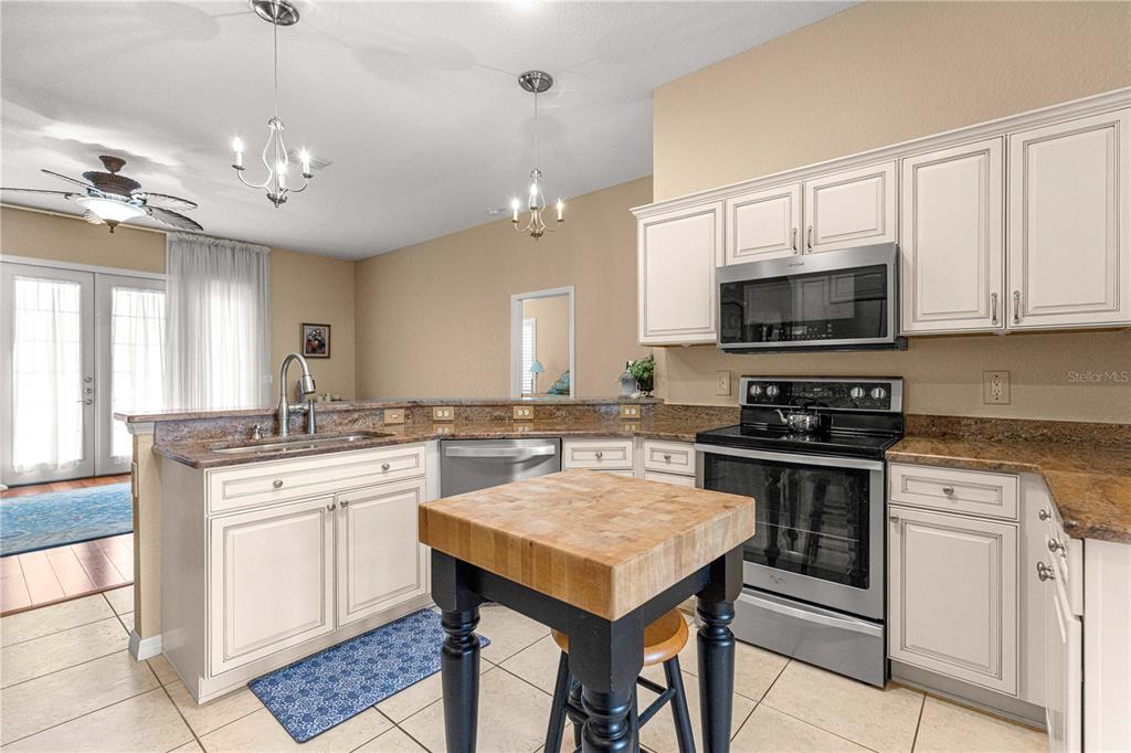 A kitchen features white cabinets, granite countertops, stainless steel appliances, and a wooden island — 12271 SE 175TH LANE, SUMMERFIELD, FL