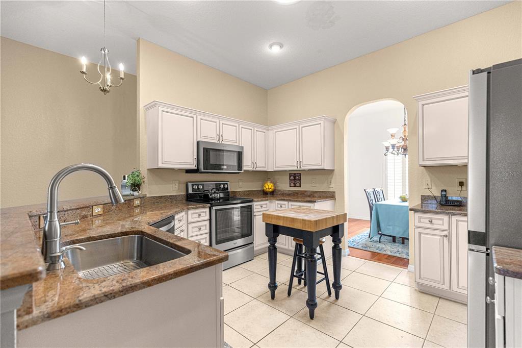 A kitchen features light-colored cabinets, granite countertops, a central island, and stainless steel appliances — 12271 SE 175TH LANE, SUMMERFIELD, FL