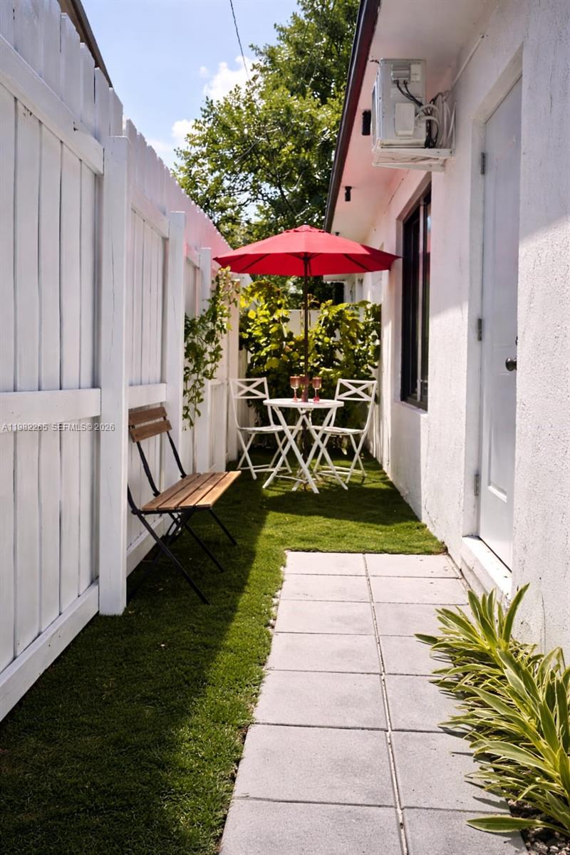 A narrow outdoor patio features a red umbrella, bistro table, chairs, and a wooden bench — 613 NW 10th St # 2, Hallandale Beach FL 33009, HALLANDALE BEACH, FL