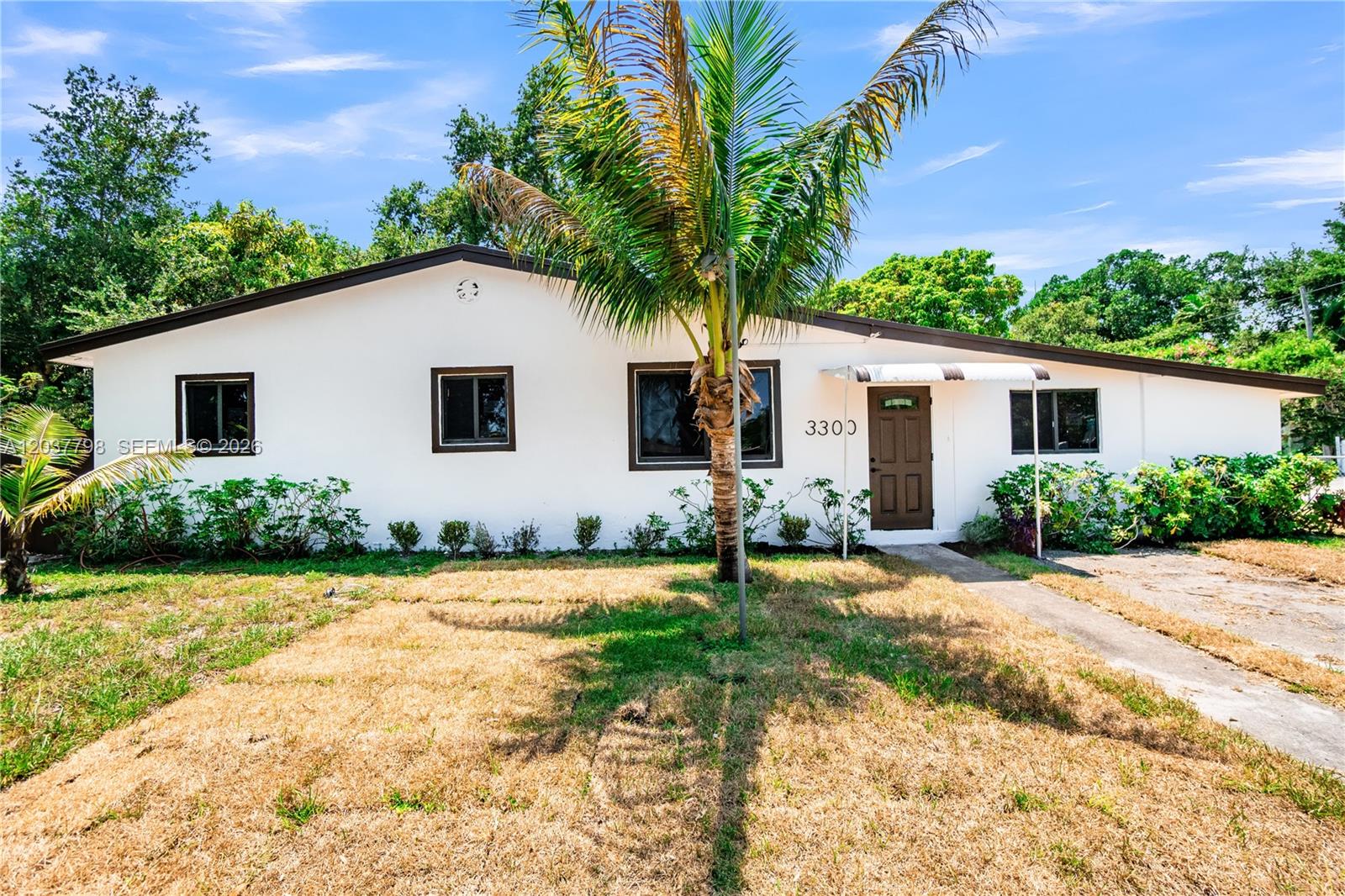 A single-story white house with a brown door, dark trim, and a palm tree out front — 3300 SW 40th Ave, West Park FL 33023, WEST PARK, FL