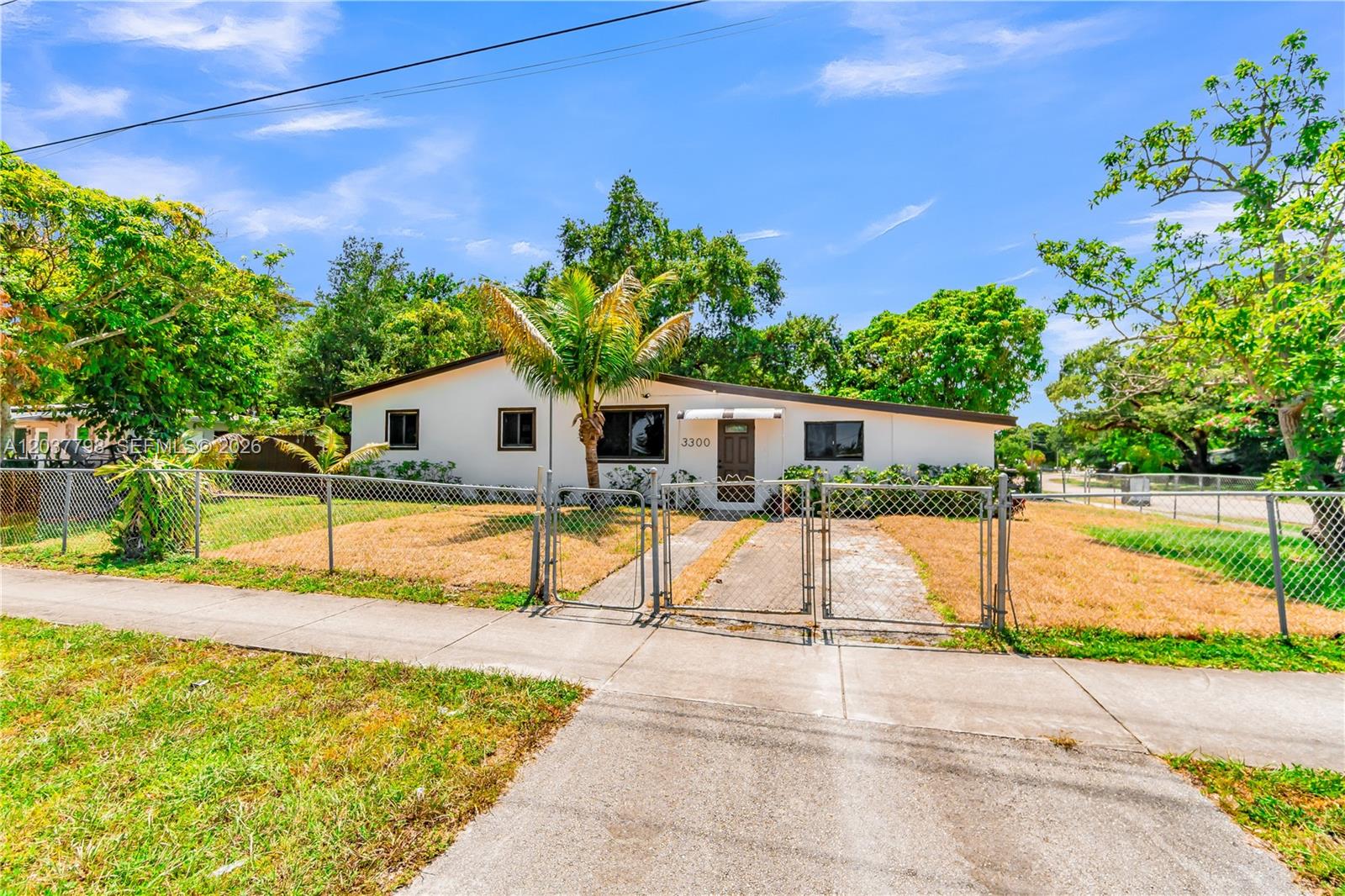 A single-story house with a white exterior, a palm tree, and a chain-link fence — 3300 SW 40th Ave, West Park FL 33023, WEST PARK, FL