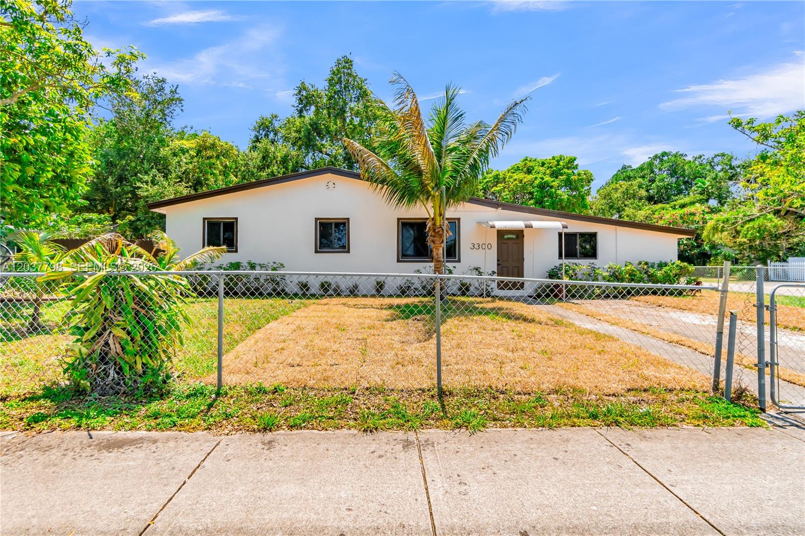 A single-story house with a white exterior, brown trim, and a chain-link fence — 3300 SW 40th Ave, West Park FL 33023, WEST PARK, FL