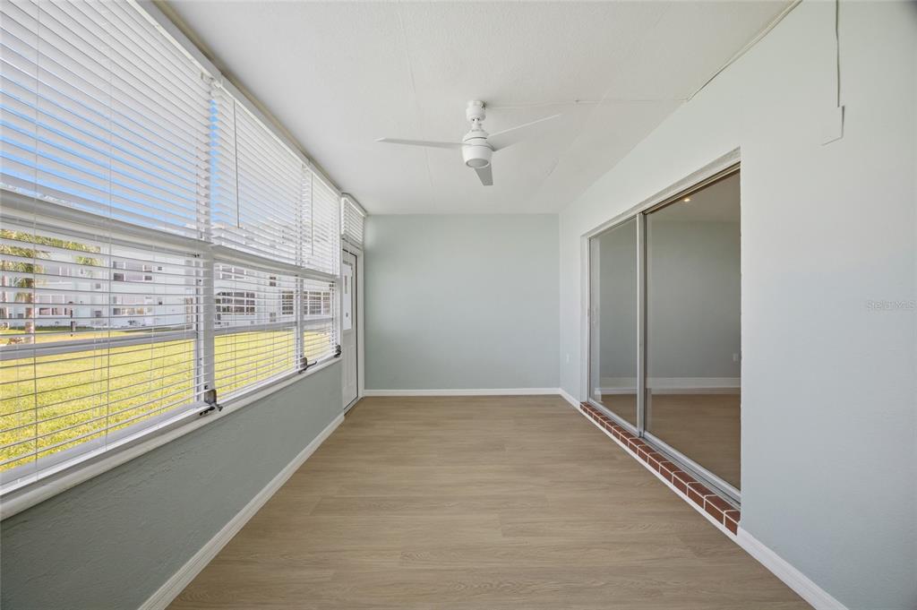A sunroom with light wood-look flooring, a ceiling fan, and large windows with white blinds — 1819 SHORE DRIVE S UNIT 103, SOUTH PASADENA, FL