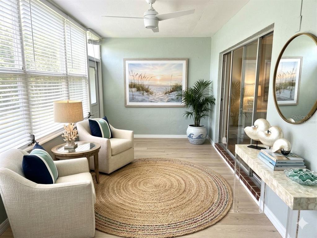A sunroom features two armchairs, a round jute rug, and a beach-themed wall print — 1819 SHORE DRIVE S UNIT 103, SOUTH PASADENA, FL