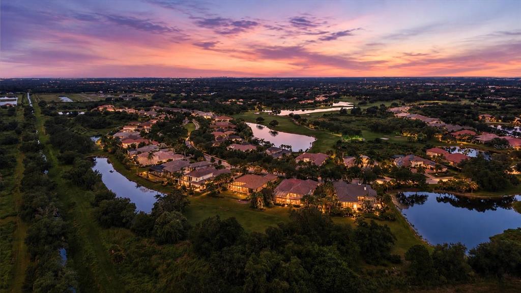 An aerial view of a residential neighborhood featuring houses, ponds, and trees at sunset — 3342 FOUNDERS CLUB DRIVE, SARASOTA, FL