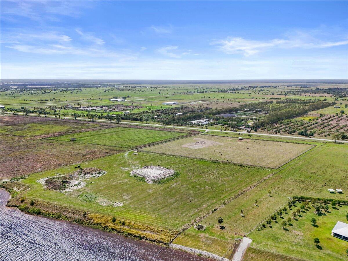 An aerial view shows a large, grassy rural property with fenced pastures and a nearby lake — 8105 SW Kanner Highway, FL 34956, FL