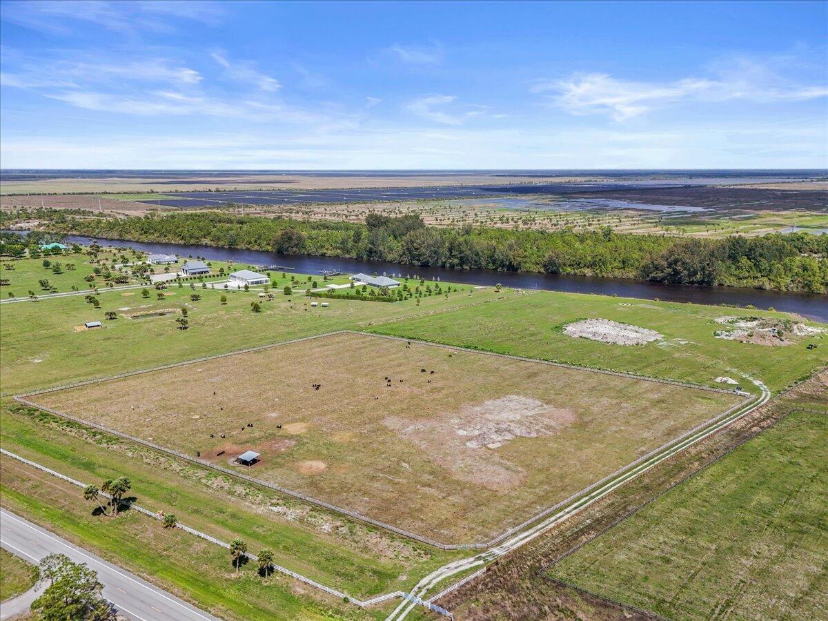 An aerial view shows a fenced pasture with cattle near a river and a road — 8105 SW Kanner Highway, FL 34956, FL