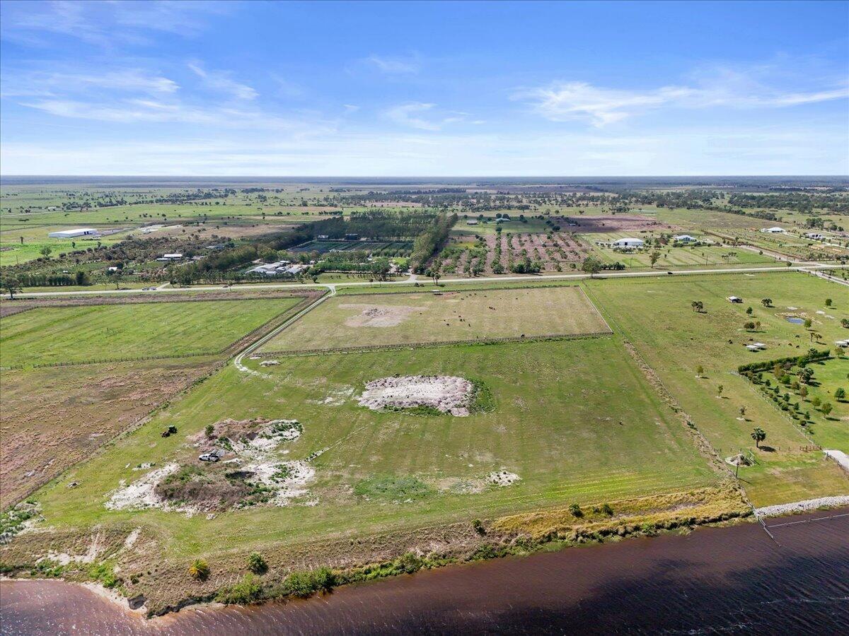 An aerial view shows a large, grassy waterfront lot with scattered dirt patches and fencing — 8105 SW Kanner Highway, FL 34956, FL