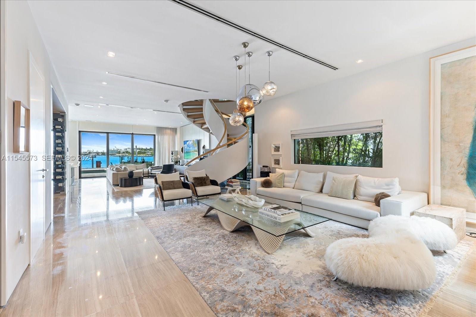 A modern living room features a spiral staircase, glass coffee table, and floor-to-ceiling waterfront windows — 401 E Rivo Alto Dr, Miami Beach FL 33139, MIAMI BEACH, FL