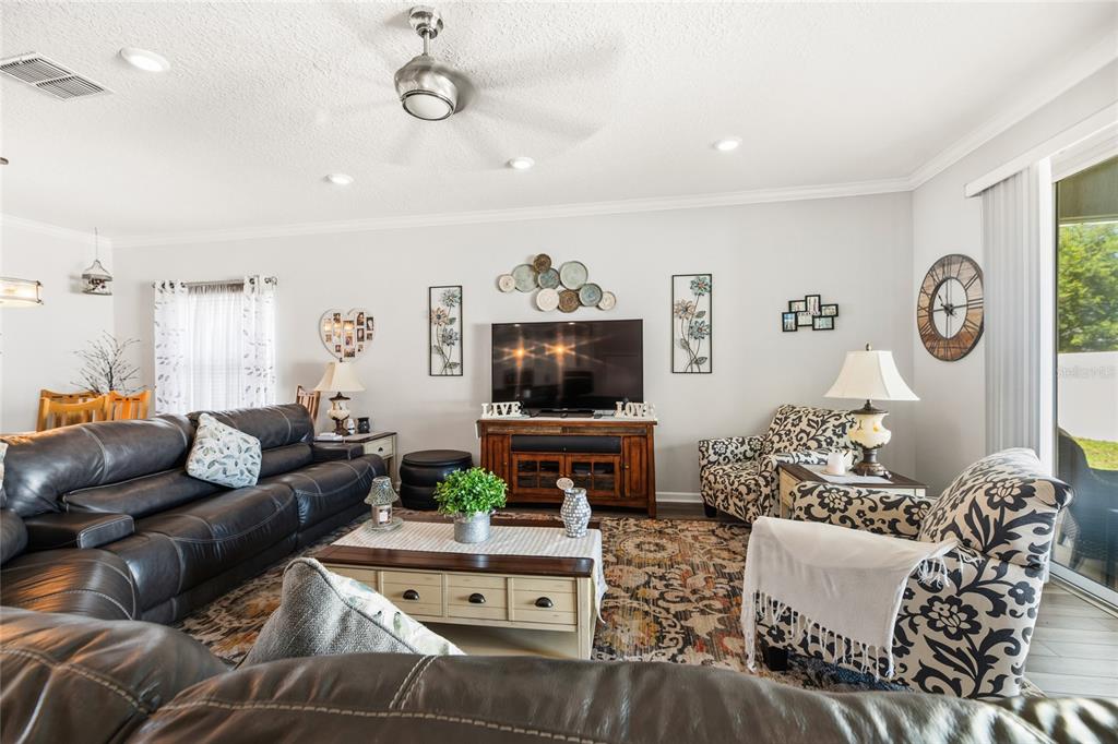 A living room features a dark leather sofa, patterned armchairs, a television console, and area rug — 31 OLIVINE COURT, ST AUGUSTINE, FL