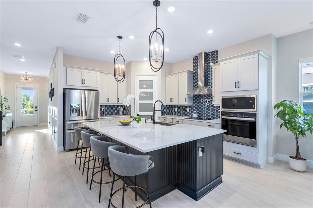 A modern kitchen features a dark island, white cabinetry, stainless steel appliances, and pendant lighting — 13373 MCMILLAN DRIVE, ORLANDO, FL
