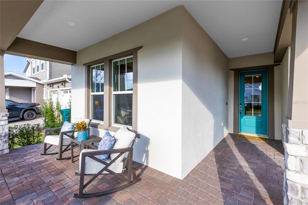 A covered front porch features brick pavers, two rocking chairs, and a teal front door — 13373 MCMILLAN DRIVE, ORLANDO, FL