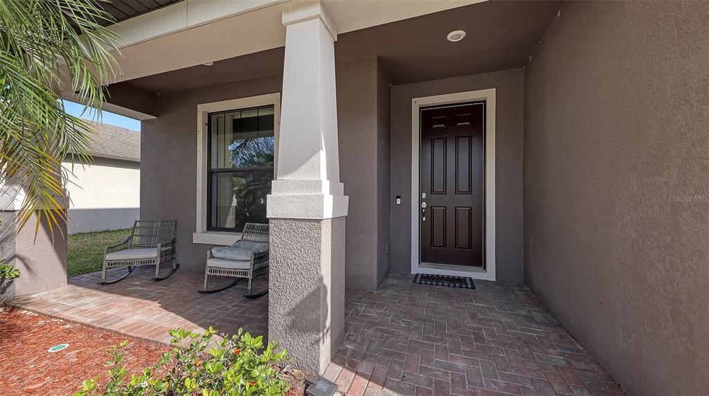 A covered brick porch features two rocking chairs, a dark front door, and a pillar — 2446 CARNATION COURT, NORTH PORT, FL