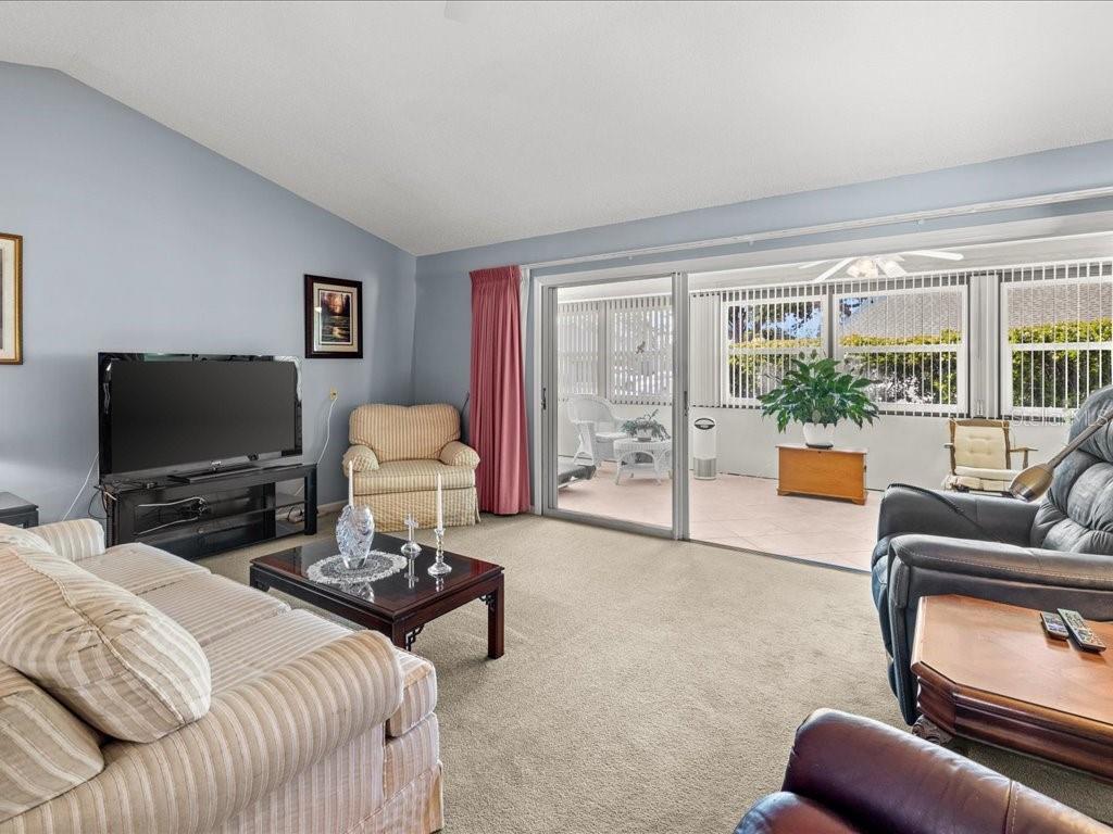A living room with beige carpet, a television, and a sliding door leading to a patio — 322 FALLING WATERS LANE UNIT 163, ENGLEWOOD, FL