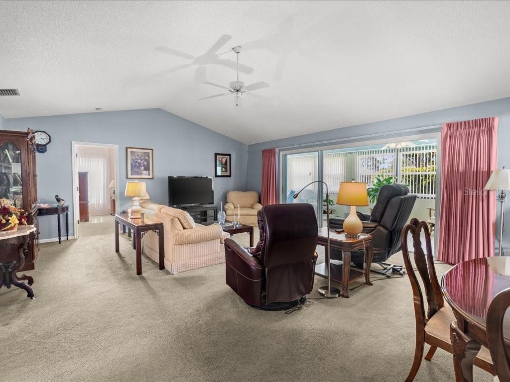 A living room with vaulted ceilings, beige carpet, a sofa, and sliding glass patio doors — 322 FALLING WATERS LANE UNIT 163, ENGLEWOOD, FL
