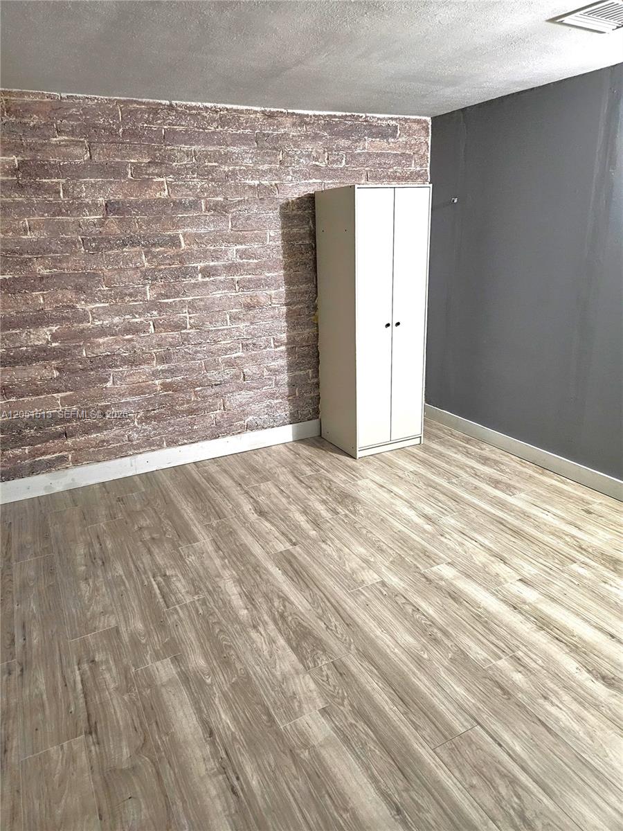 A room features a brick accent wall, light wood-look flooring, and a white freestanding wardrobe — 5627 SW 26th St # 0, West Park FL 33023, WEST PARK, FL