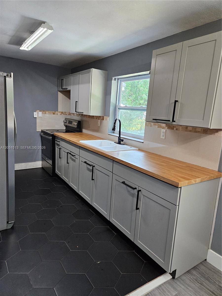 A kitchen features gray cabinets, a wooden countertop, a white sink, and black hexagonal flooring — 5627 SW 26th St # 0, West Park FL 33023, WEST PARK, FL